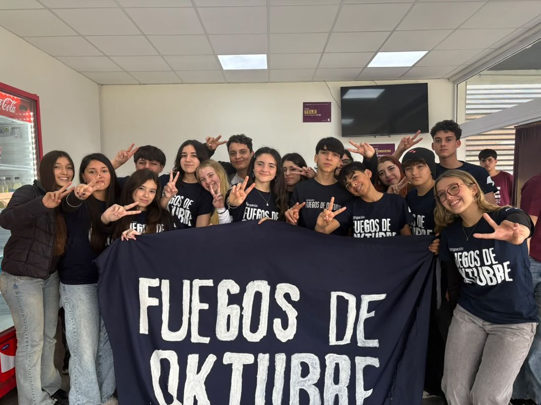 Integrantes de Fuegos de Oktubre con remeras de la agrupación sosteniendo la bandera