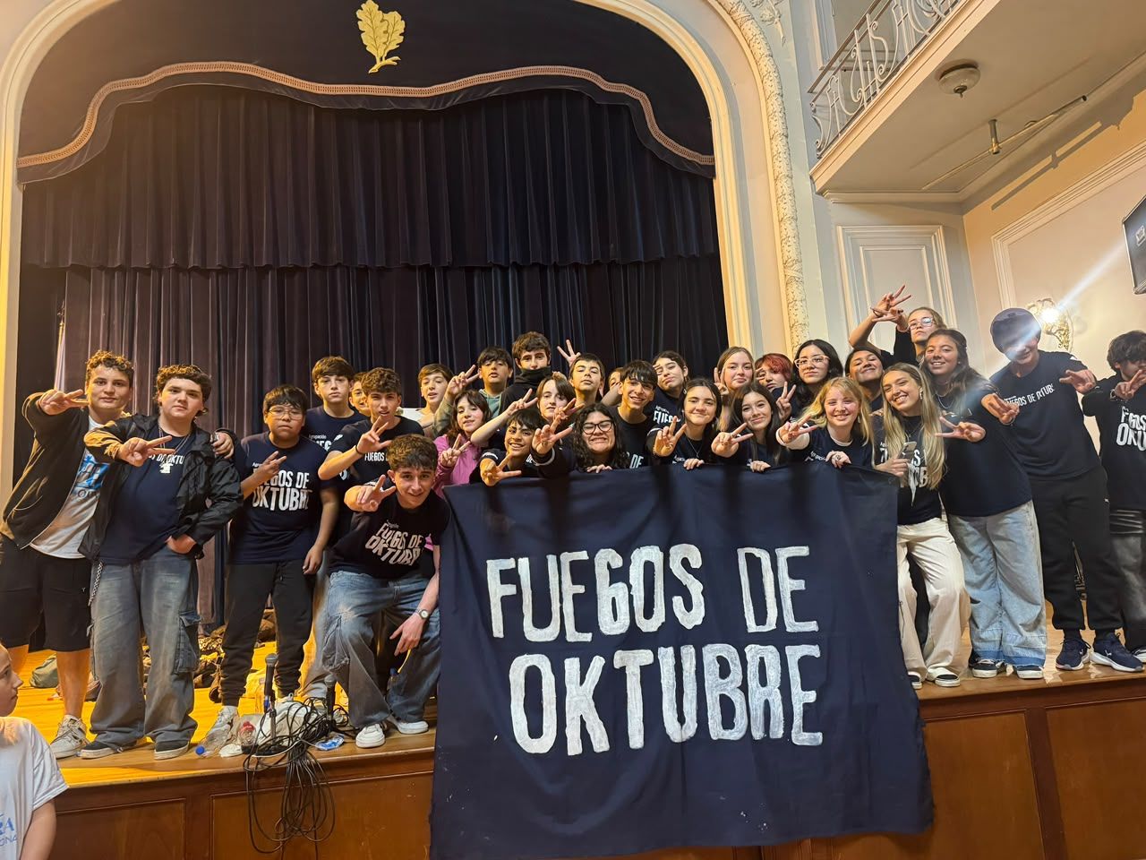 La agrupación festejando sobre el escenario del salón de actos con la bandera de Fuegos de Oktubre